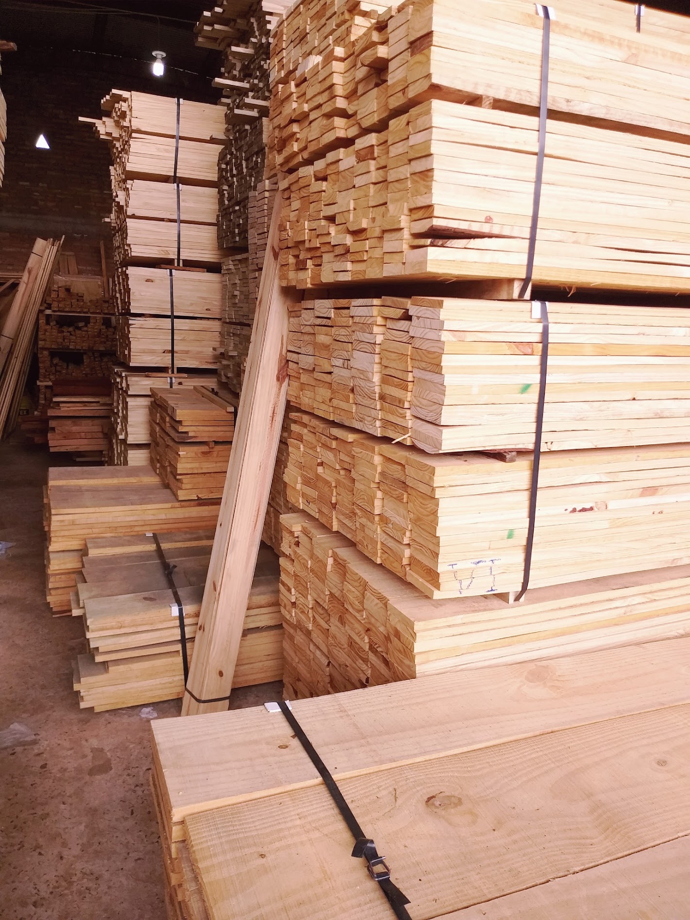 Almacén con vigas y tablones de madera apilados, estructuras de marco y luces de techo.